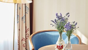 Una habitación de hotel con una mesa redonda de madera, dos jarrones con flores, un osito de peluche y una lámpara.
