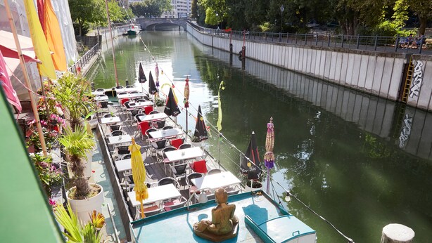 Un restaurante junto al río con terraza al aire libre, una estatua y vistas del río.