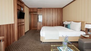 Una habitación de hotel con una cama grande, un armario de madera, un televisor y una pequeña mesa con un florero.