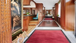 Un pasillo con paneles de madera, alfombra roja y un cuadro a la izquierda.