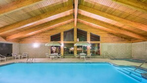 Une piscine intérieure avec des poutres en bois, des murs carrelés et un espace extérieur aménagé pour se détendre.