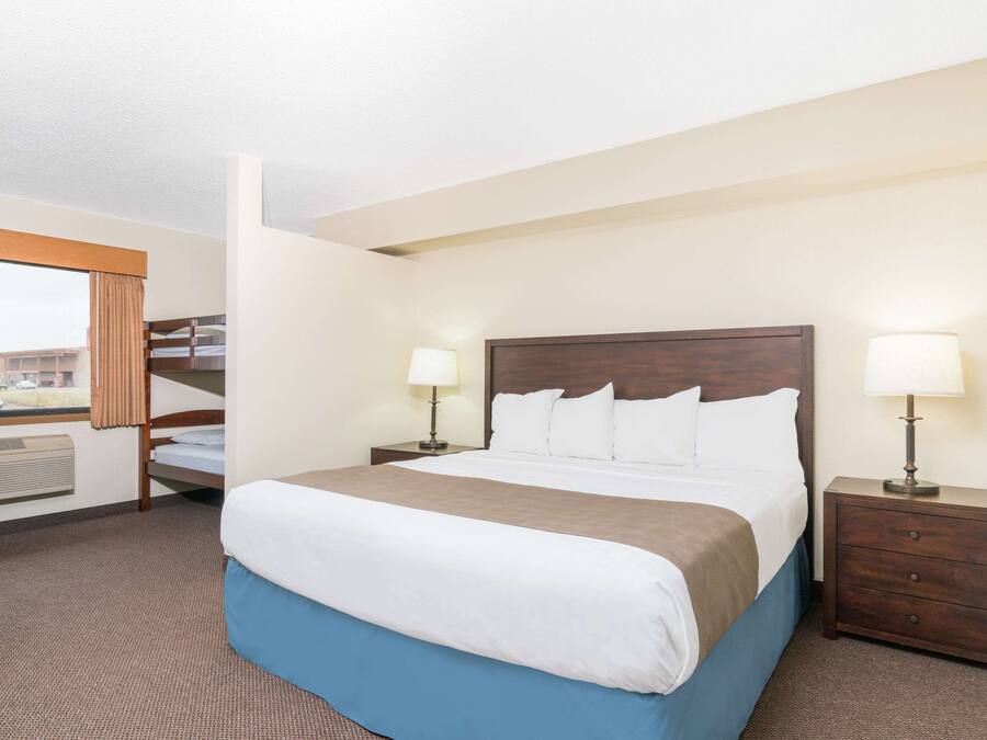 A hotel room with a large bed, two bedside tables with lamps, a window with curtains, and a view of the outside.
