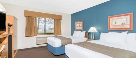 Quarto de hotel com duas camas, uma mesa de trabalho com televisão e uma janela com cortinas.
