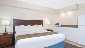 A hotel room with a bed, bedside tables, a lamp, a microwave, and a refrigerator.