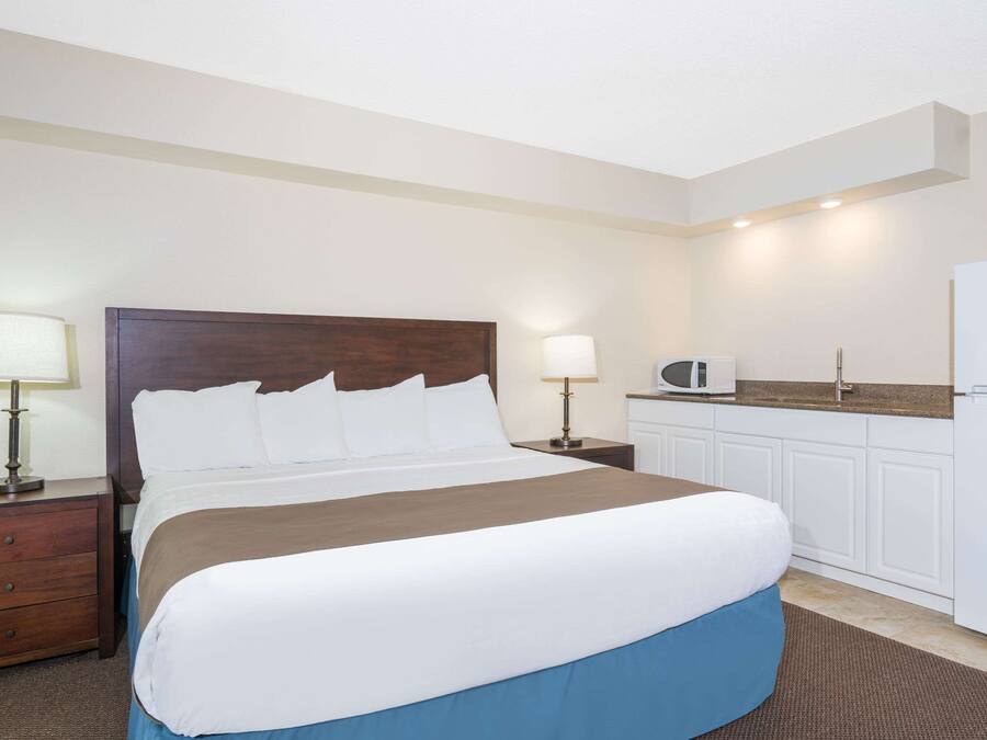 A hotel room with a bed, bedside tables, a lamp, a microwave, and a refrigerator.