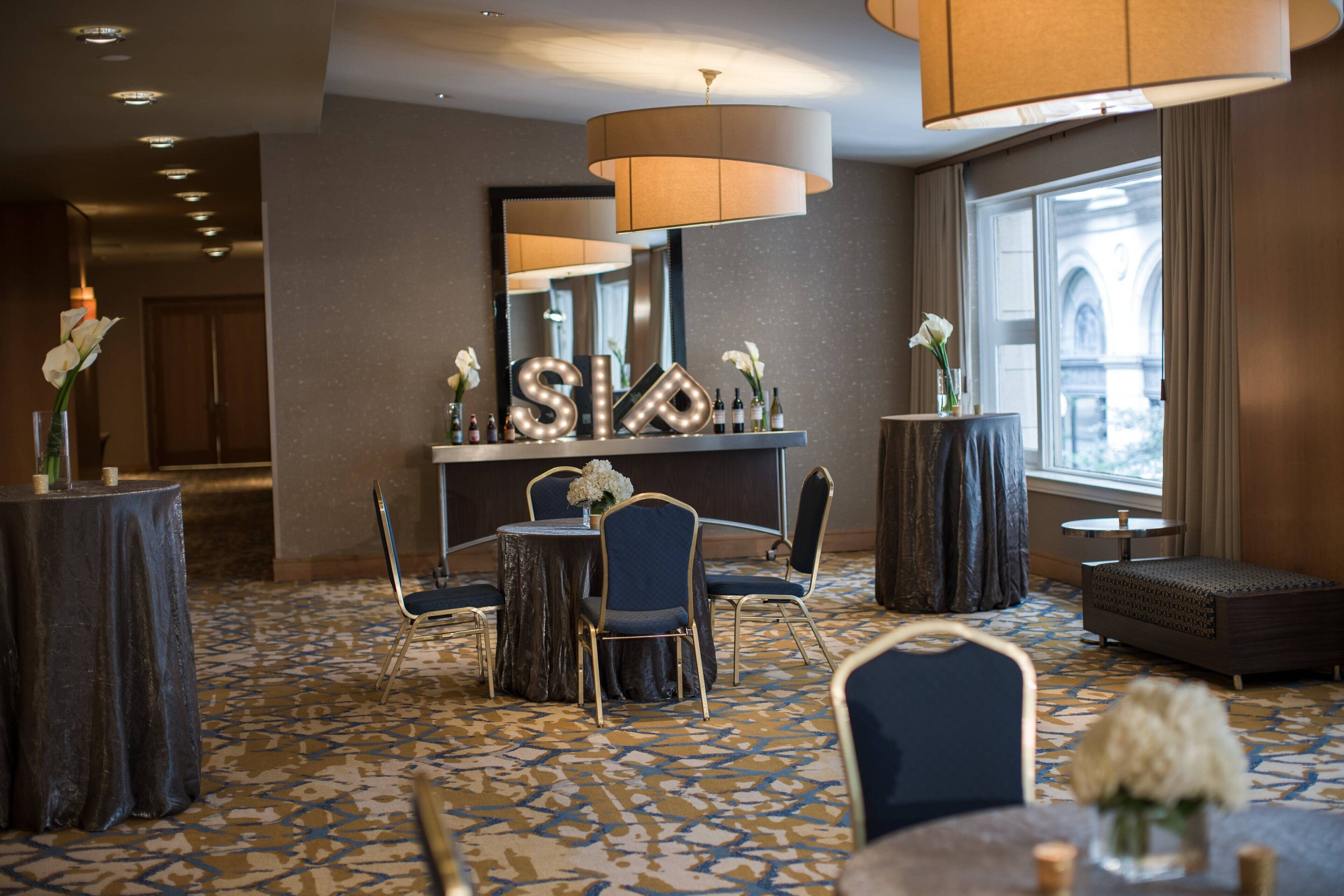 A hotel lobby with a round table, chairs, a sofa, a mirror, and a large window with curtains.