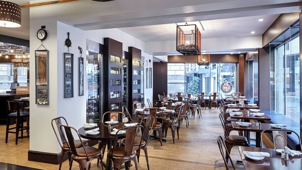 Un restaurante espacioso con mesas y sillas de madera, un ventanal con vistas a la ciudad y una lámpara moderna.