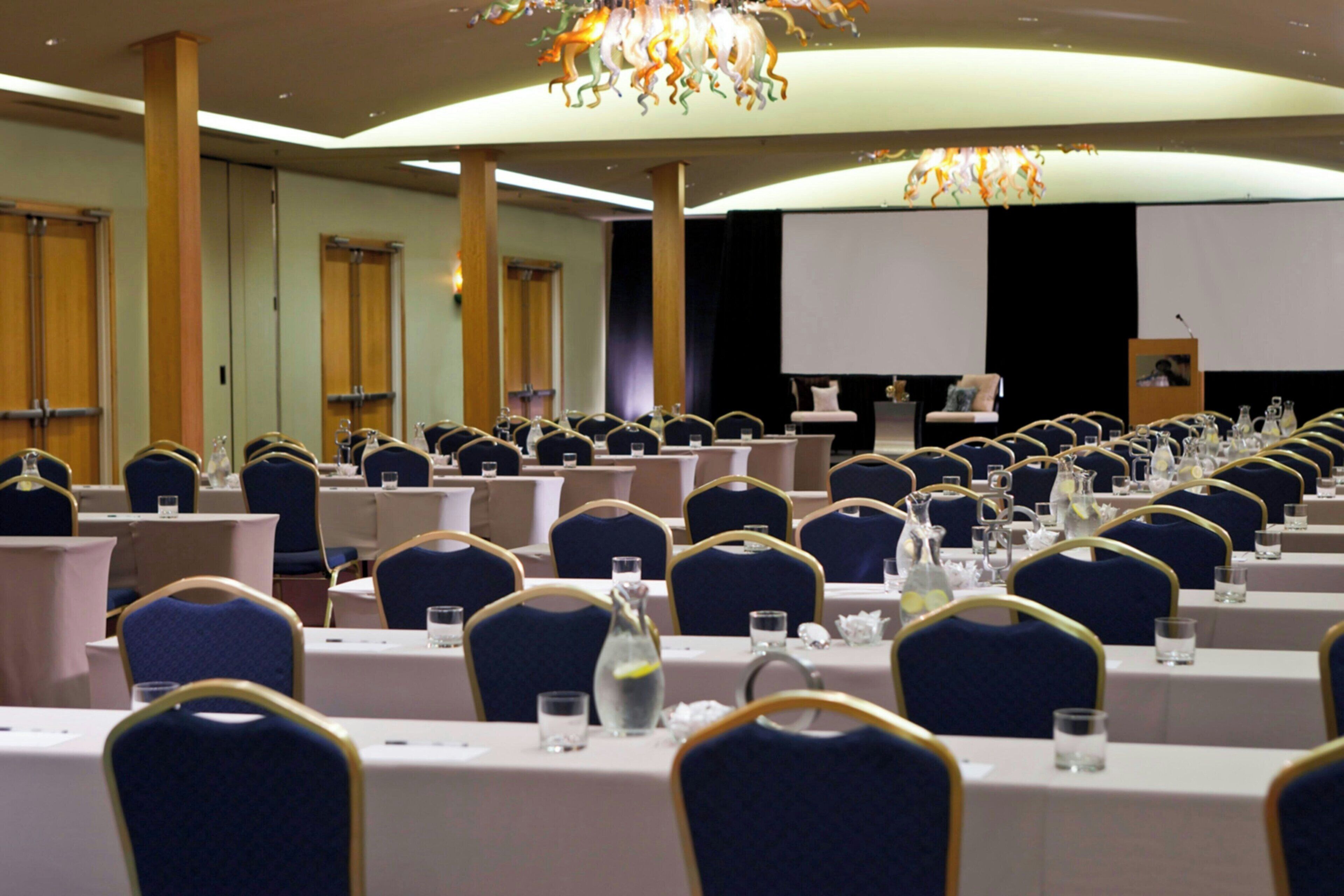 A conference room with rows of tables, chairs, and a large screen at the front.