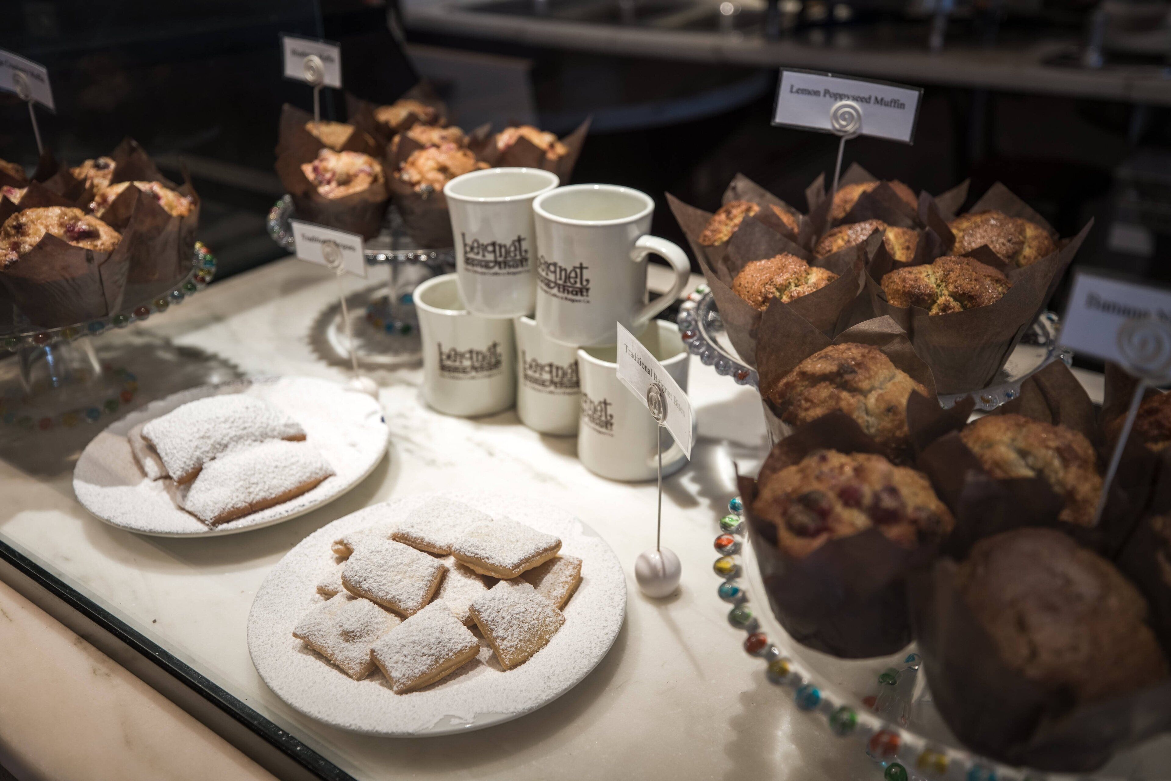 A display of baked goods including muffins and cookies, with labels indicating different flavors.