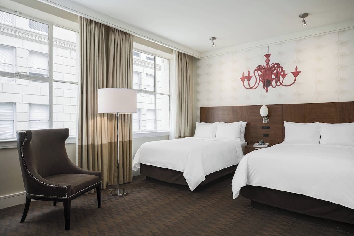 Een hotelkamer met twee bedden, een stoel, een lamp en een kroonluchter.
