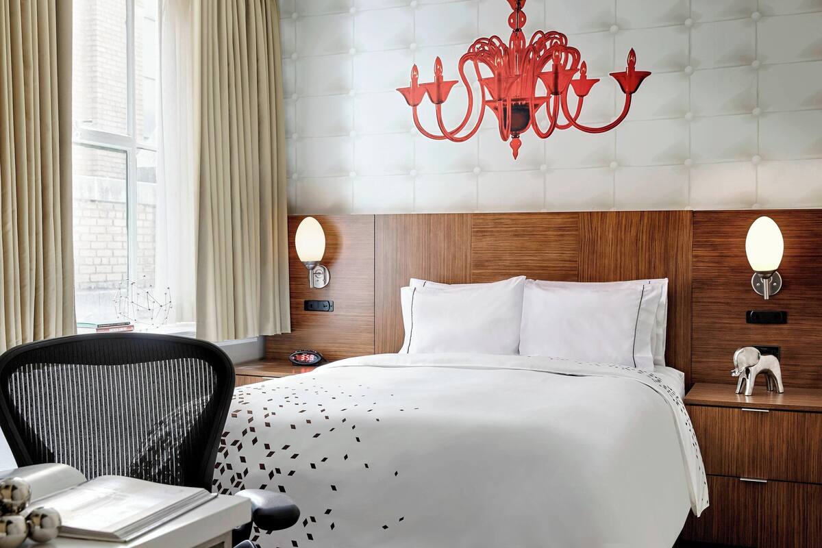 Een hotelkamer met een bed, een bureau met stoel, een kroonluchter en een nachtkastje met een klok.