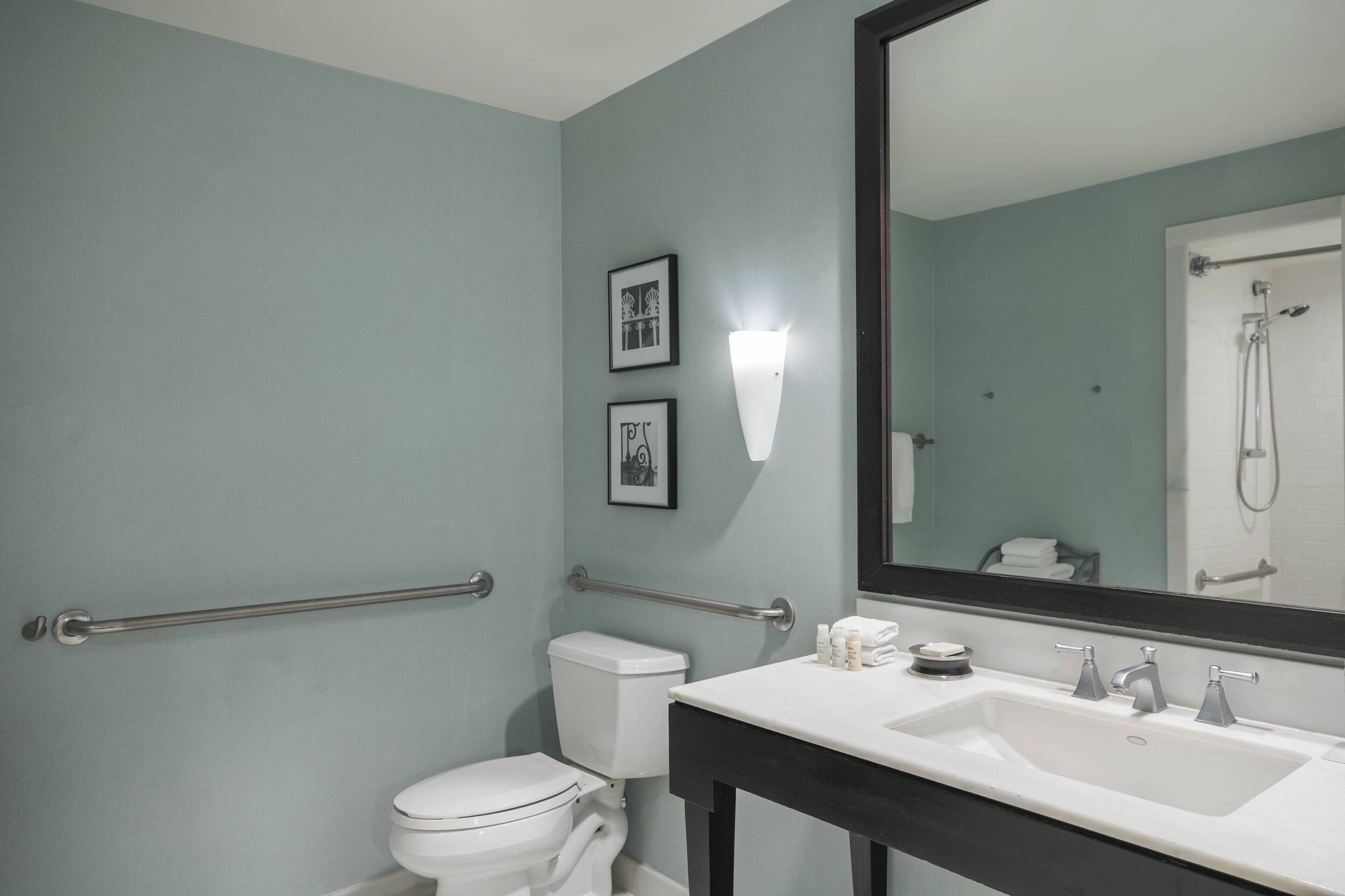 A bathroom with a white sink, two faucets, a mirror, and a toilet.