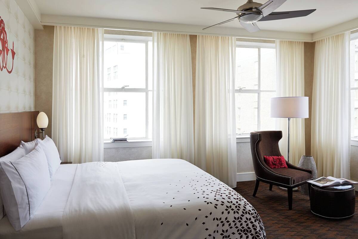 Een hotelkamer met een groot bed, een stoel, een lamp en een raam met gordijnen.
