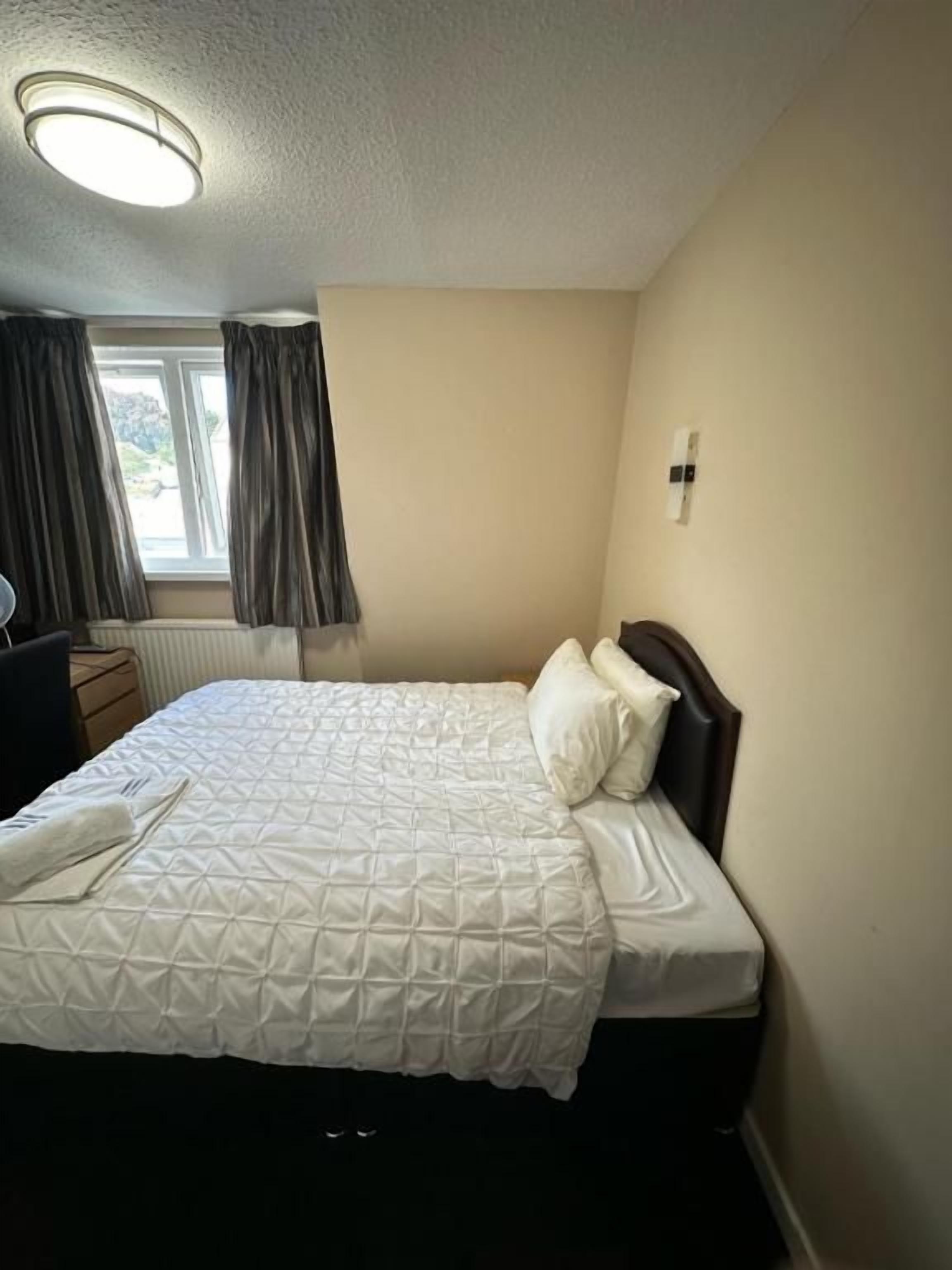 Een hotelkamer met een bed, nachtkastje, lamp en raam met gordijnen.