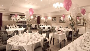 Un salón de banquetes con mesas redondas dispuestas para cenar, globos y una zona de bar al fondo.