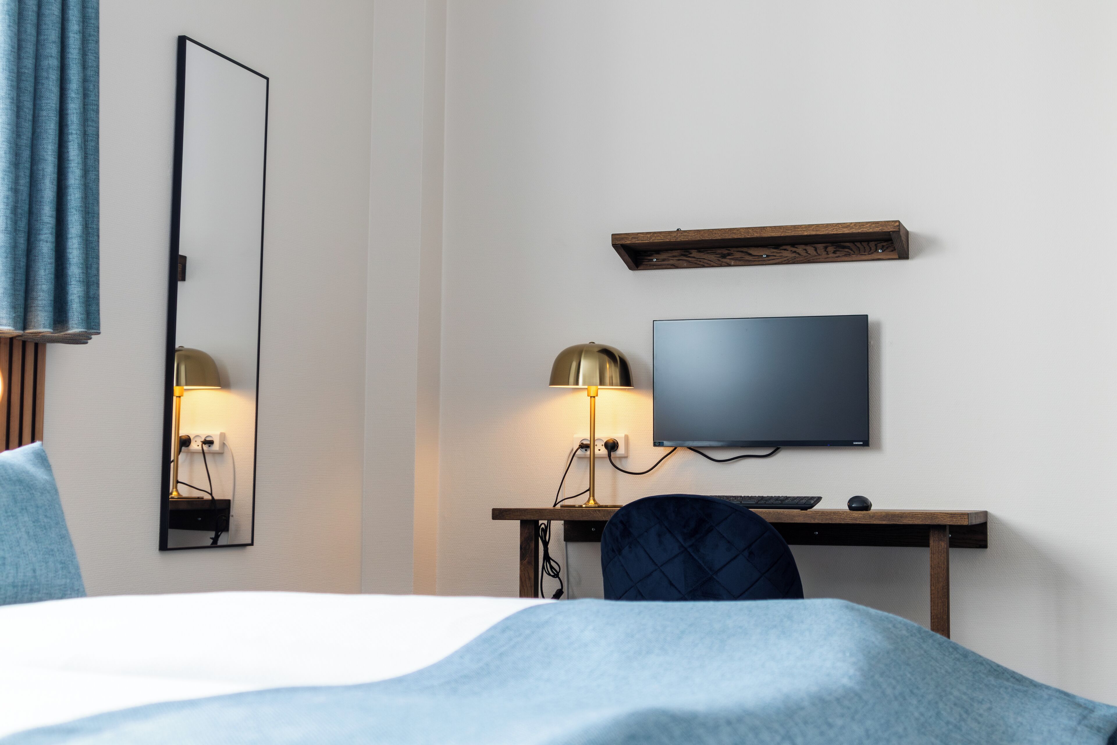 A hotel room with a bed, a desk with a computer, a TV, and a mirror.