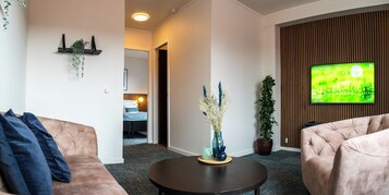 Una sala de estar moderna con un sofá, una mesa de centro y un televisor mostrando una escena natural.