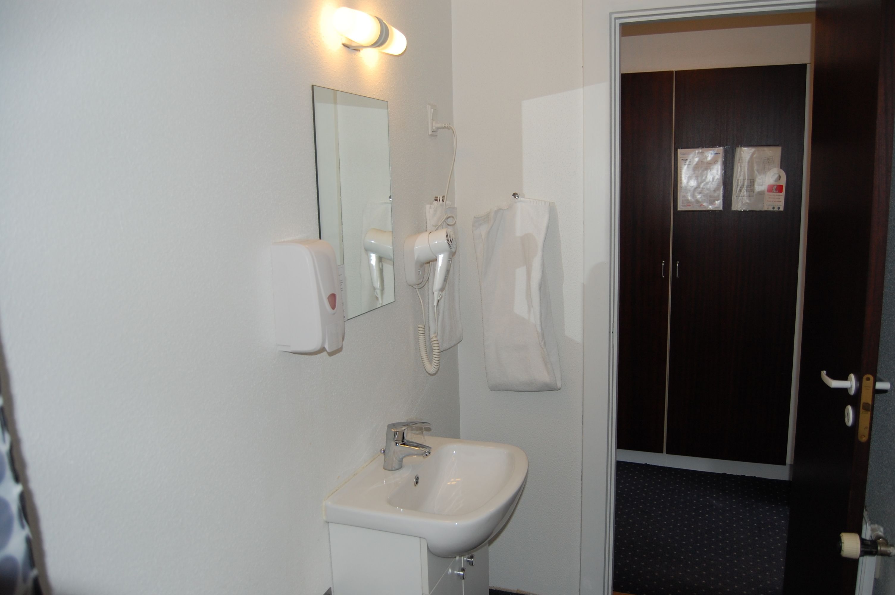 Ein Badezimmer mit Waschbecken, Spiegel, Haartrockner und Handtuchhalter.
