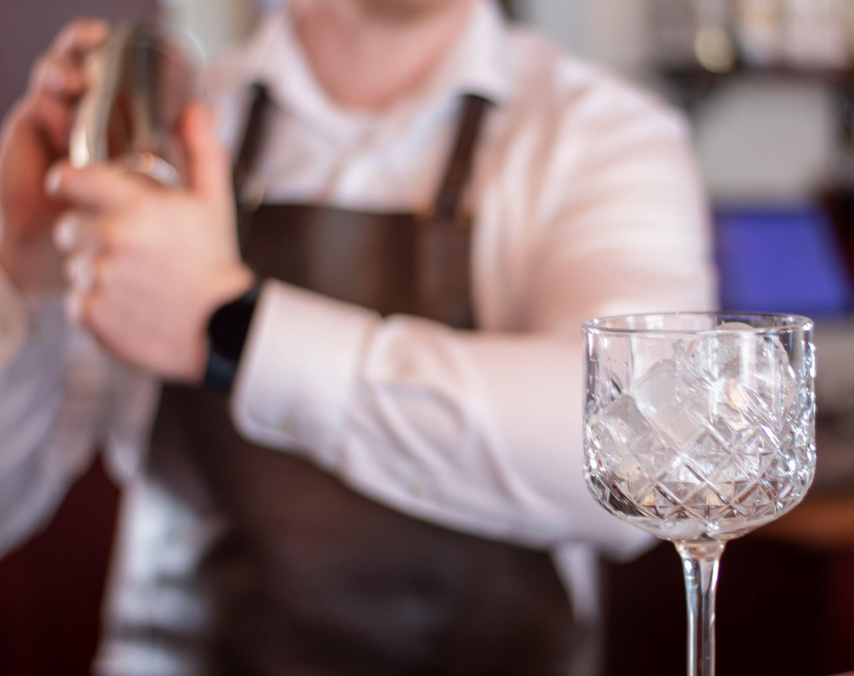 Een bartender maakt een drankje, met een helder glas op de voorgrond.