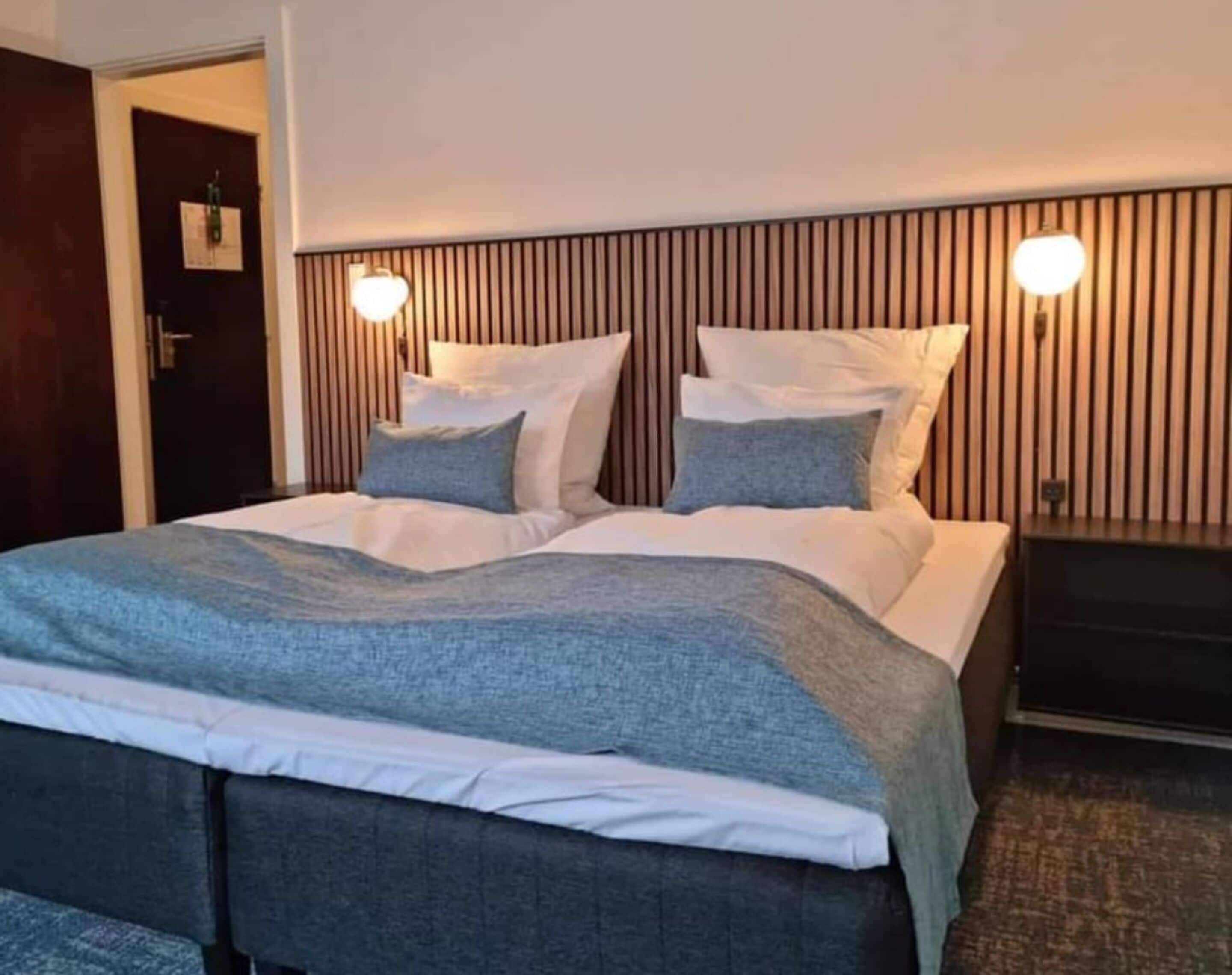 Une chambre d’hôtel avec un lit, une tête de lit à lattes verticales et deux lampes fixées au mur.