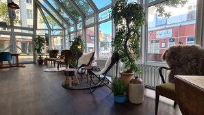 Interior de una cafetería con amplios ventanales, muebles de madera y plantas en macetas.