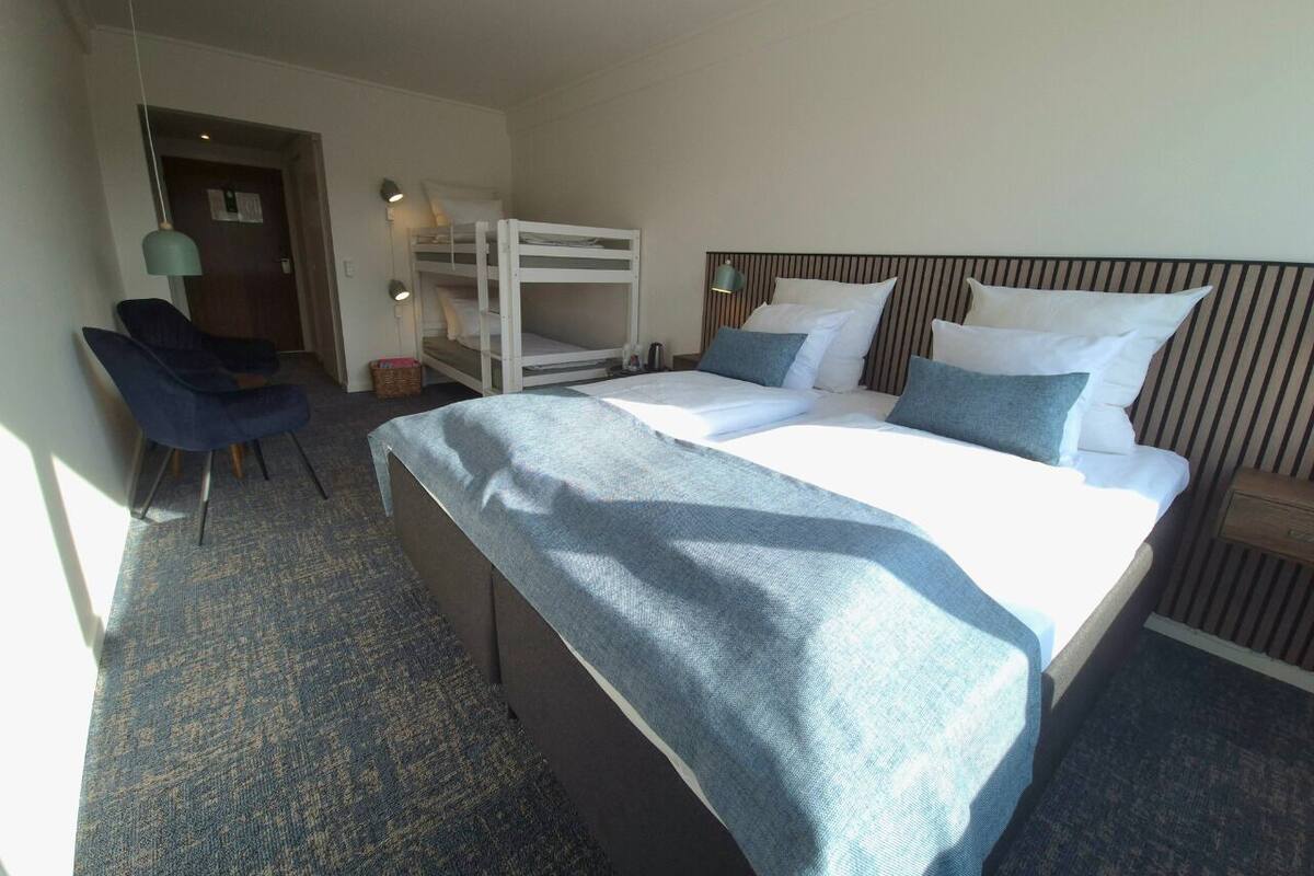 A hotel room with a large bed, a desk, a chair, and a bunk bed.