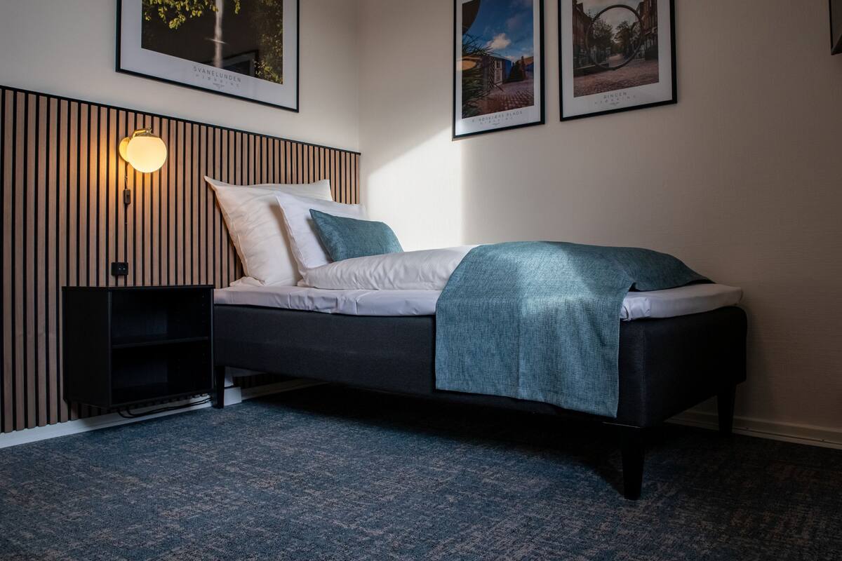 A modern bedroom with a bed, a wall-mounted light, and framed pictures.