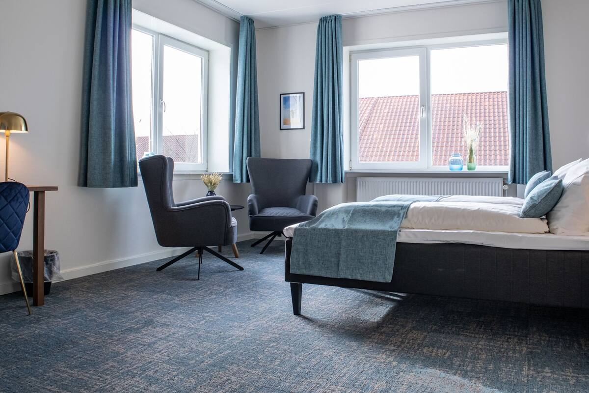 A modern hotel room with a bed, a desk, a chair, and a window with curtains.