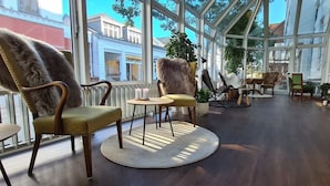 Amplio espacio interior con grandes ventanales, piso de madera y diferentes distribuciones de asientos, incluyendo sillas y un sofá.