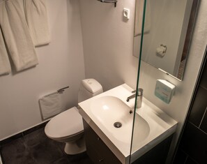 Un baño moderno con inodoro blanco, lavamanos con mampara de vidrio y espejo.