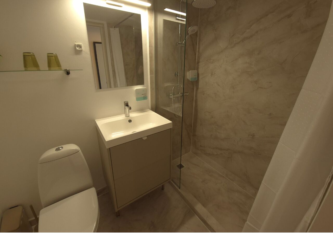 Un baño con inodoro, lavamanos, espejo y ducha con mampara de vidrio.