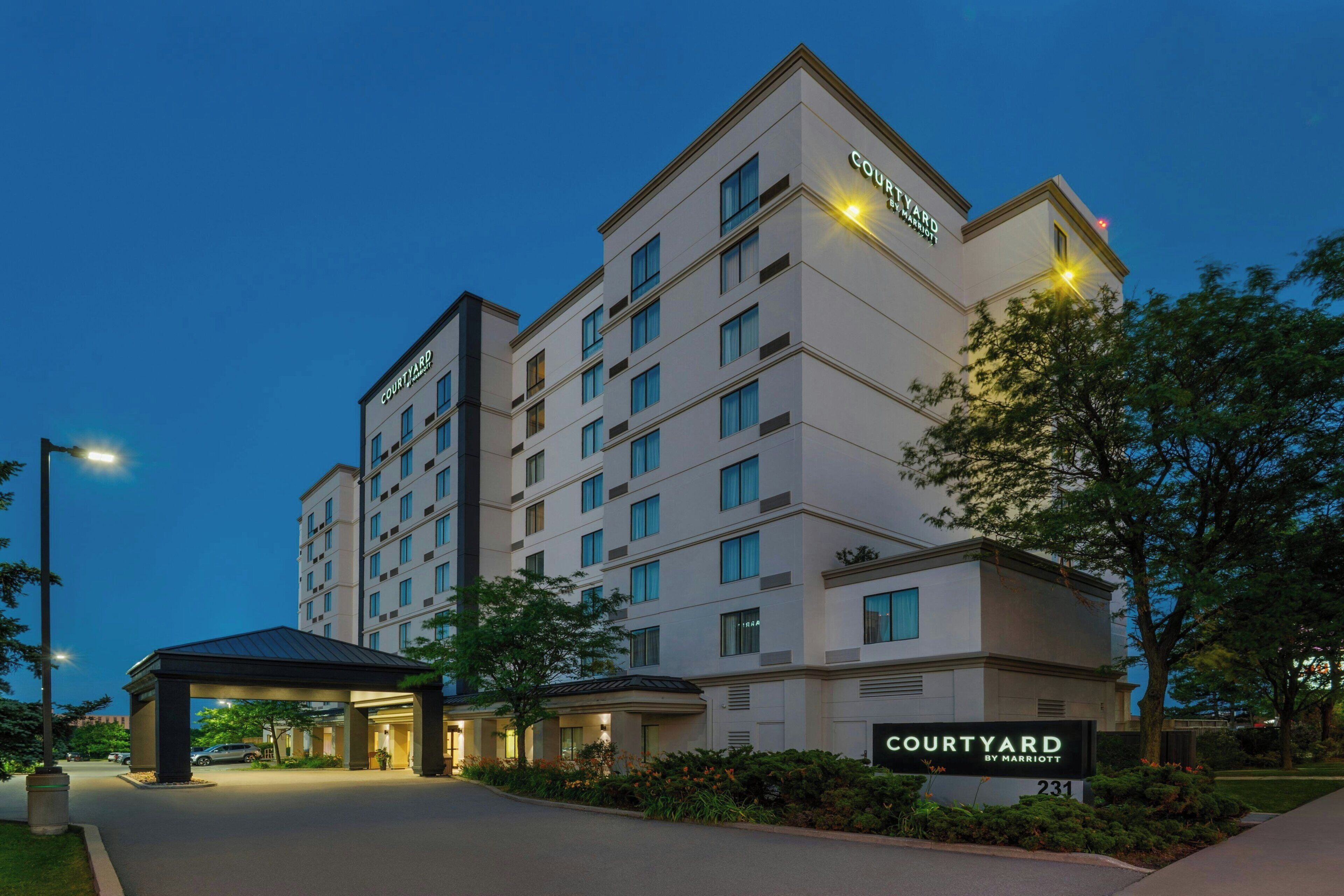 Un hotel de varios pisos con un llamativo letrero de 'Courtyard by Marriott', una entrada cubierta y una fachada bien iluminada.