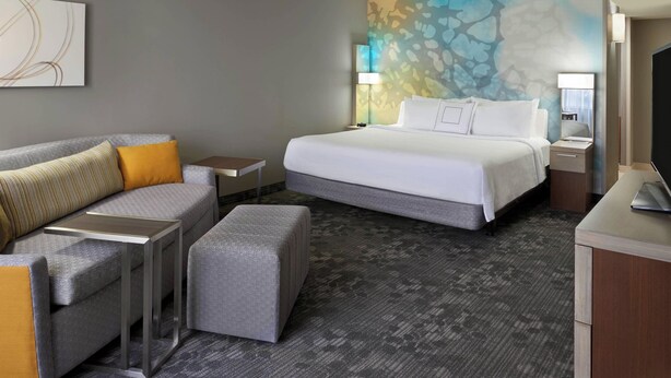 Una habitación de hotel con cama, sofá, una mesita, lámpara y televisor.