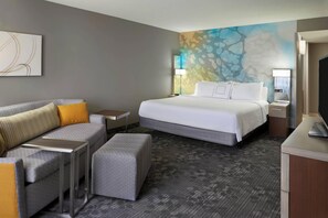 A hotel room with a bed, a sofa, a small table, a lamp, and a TV. - Courtyard by Marriott Toronto Airport (Toronto)