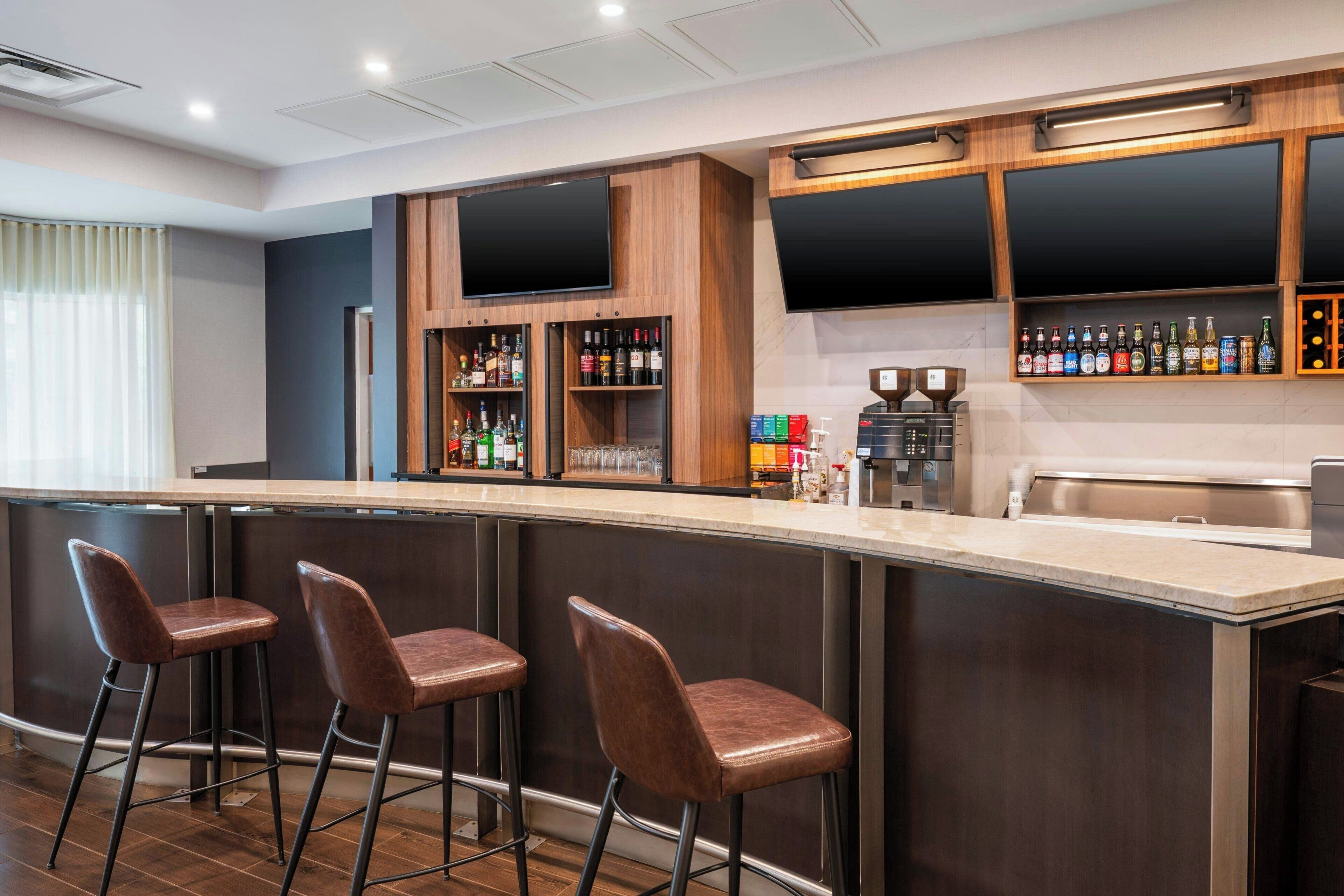 A bar area with a long counter, three bar stools, shelves with bottles, and a coffee machine.