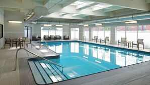 Una piscina interior con agua cristalina, rodeada de sillones reclinables y mesas.