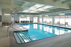 Una piscina interior con agua cristalina, rodeada de sillones reclinables y mesas.