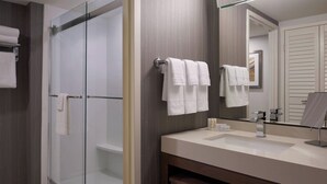 Un baño moderno con ducha envuelta en vidrio, tocador con lavamanos y un espejo grande.
