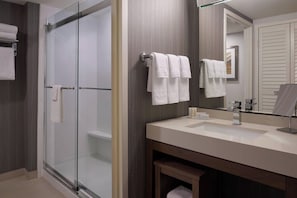 Un baño moderno con ducha envuelta en vidrio, tocador con lavamanos y un espejo grande.