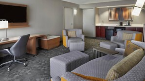 Habitación de hotel con escritorio, dos sillones, sofá, televisor, zona de cocina y mesa de comedor.