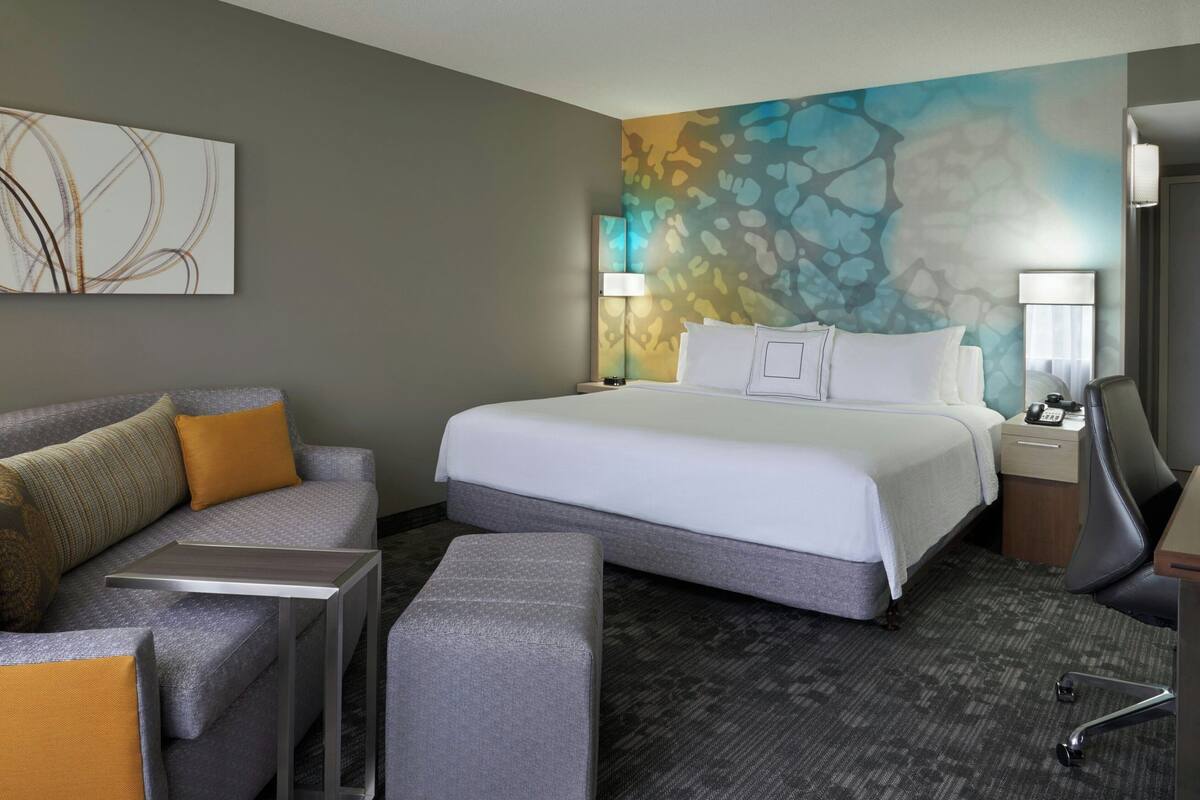 A hotel room with a bed, a sofa, a desk, and a lamp.