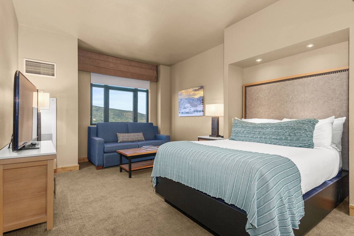 A hotel room with a bed, a sofa, a desk, a lamp, and a painting on the wall.