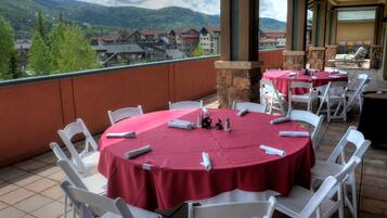 A terrace with round tables covered in red tablecloths, white chairs, and stone pillars.
