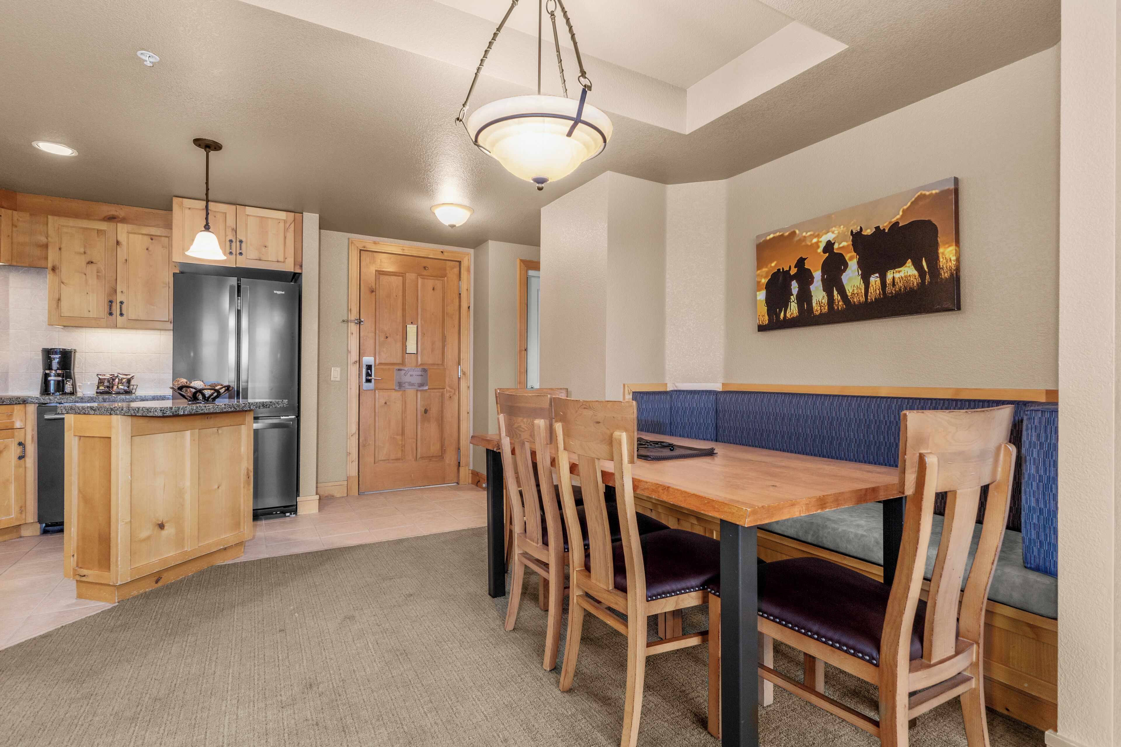 A kitchen with wooden cabinets, a stainless steel refrigerator, and a dining area with a wooden table and chairs.