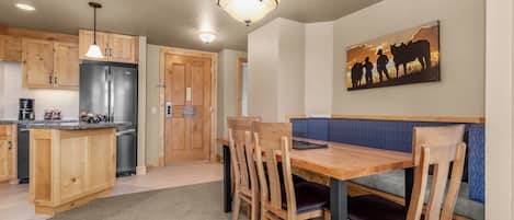 A kitchen with wooden cabinets, a stainless steel refrigerator, and a dining area with a wooden table and chairs.