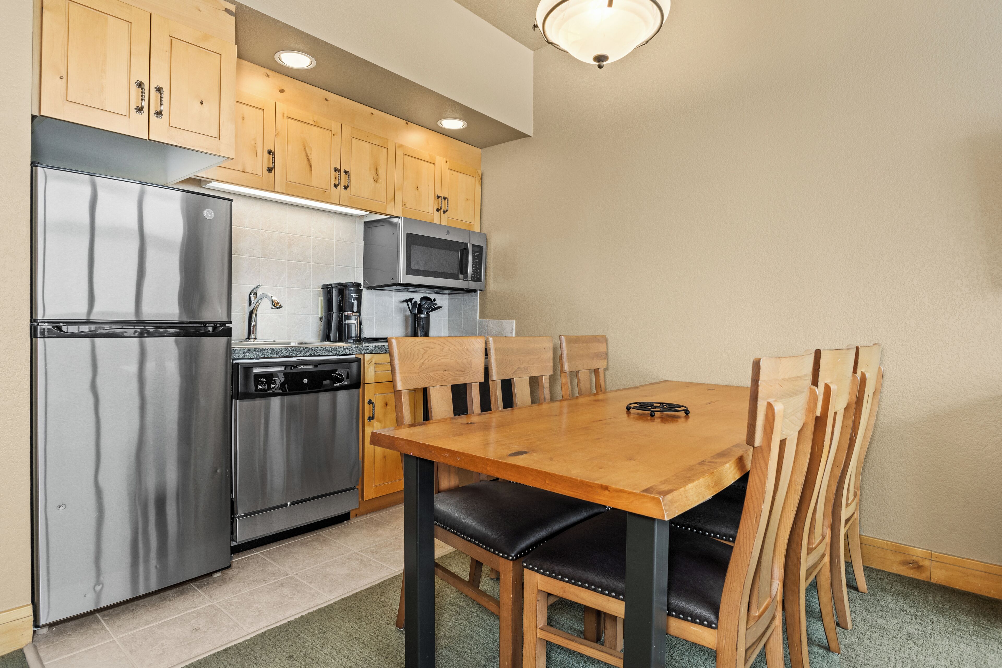 Una cocina compacta con electrodomésticos de acero inoxidable, armarios de madera y una mesa de comedor con sillas.