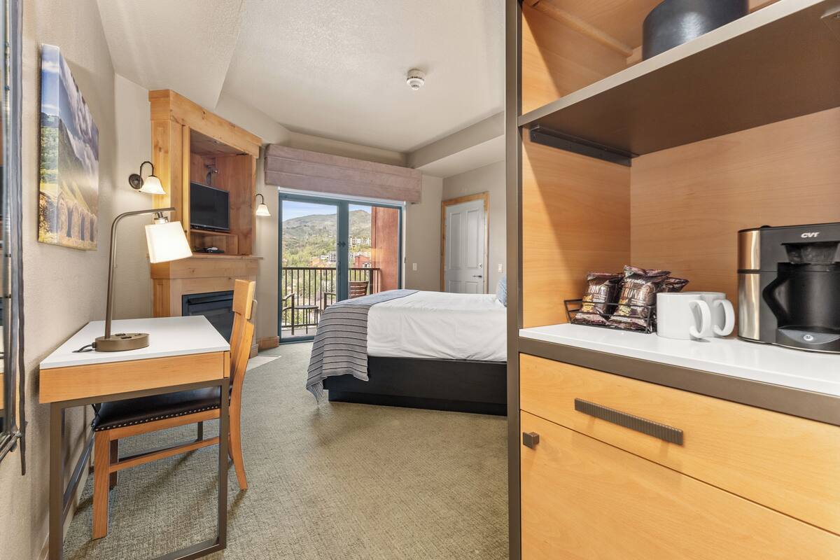 A hotel room with a bed, a desk with a chair, a coffee maker, and a TV.