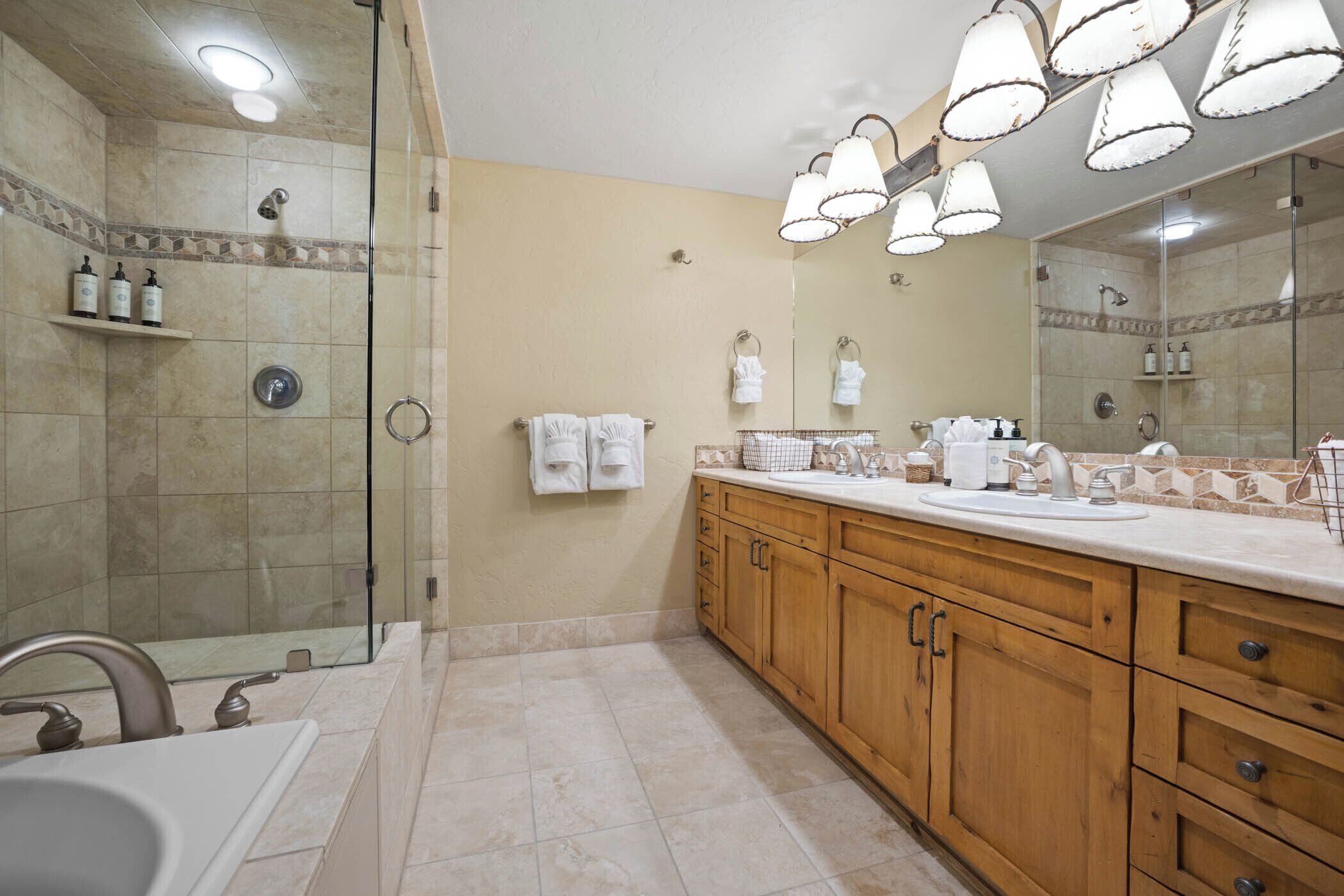 A modern bathroom with a glass-enclosed shower, a large mirror, wooden cabinets, and a white sink.