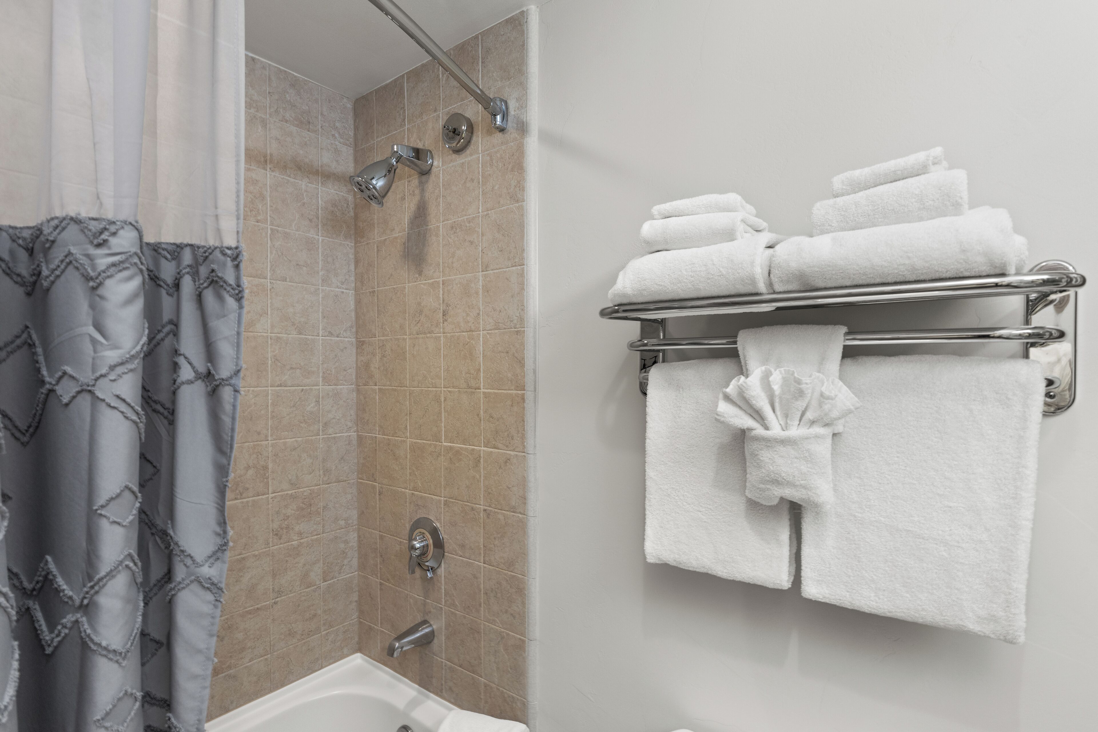 A bathroom with a shower, a bathtub, and a towel rack with folded towels.