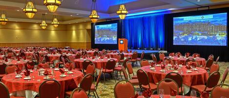 A banquet hall with round tables set for a formal event, a stage with a large screen, and a podium.